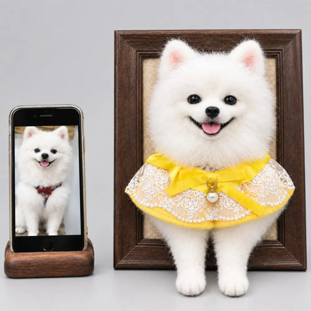 Custom 3D felted white Pomeranian portrait in a dark wooden frame, wearing a yellow lace collar beside its reference photo.