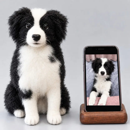 Custom felted black and white Border Collie sculpture sitting upright beside the reference pet photo displayed on a phone.