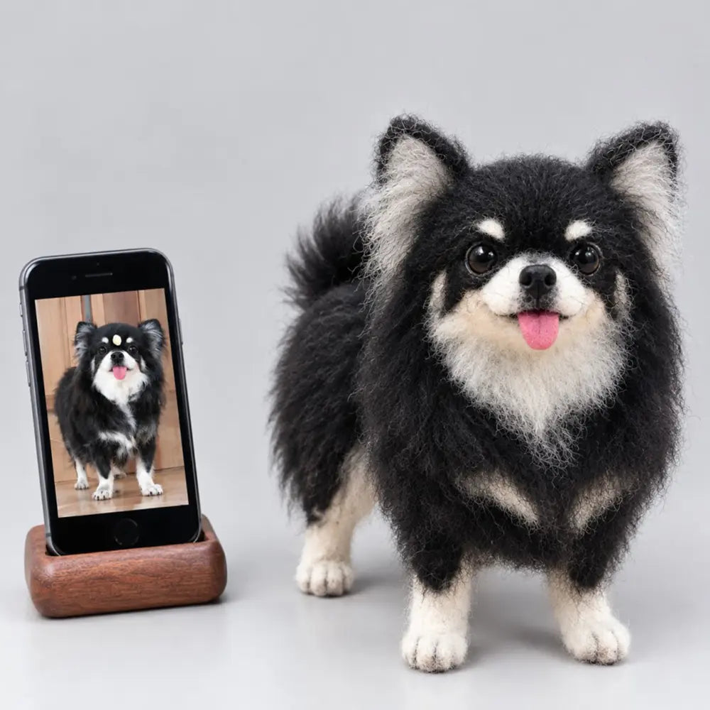 Custom felted long-haired Chihuahua sculpture with black fur, cream markings and a pink tongue, beside the reference photo on a phone.