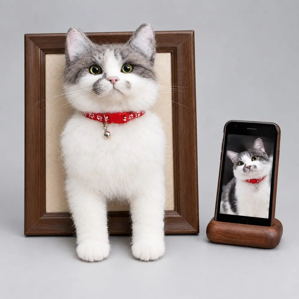 Custom 3D needle felted grey and white cat wearing a red floral collar with a bell in a wooden frame next to its smartphone photo reference